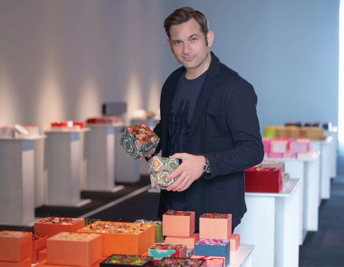 Flower artist Nicolai Bergmann holding a flower box in his hand being surrounded by a variety of different flower boxes. 